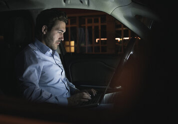 Young man using laptop in car at night - UUF17604
