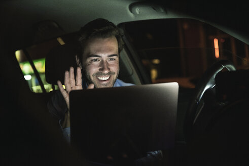 Glücklicher junger Mann bei einer Videokonferenz im Auto bei Nacht - UUF17611