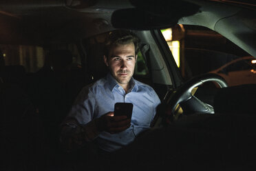 Young man using cell phone in car at night - UUF17613