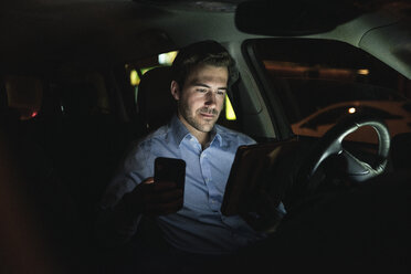 Young man using cell phone and tablet in car at night - UUF17614