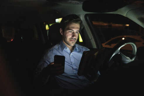 Junger Mann benutzt Handy und Tablet im Auto bei Nacht - UUF17614
