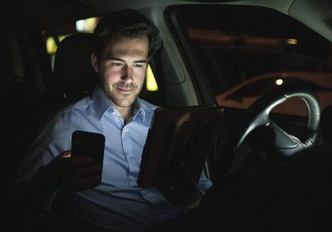 Junger Mann benutzt Handy und Tablet im Auto bei Nacht - UUF17615