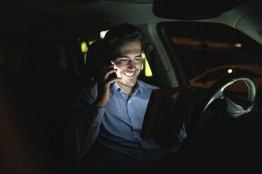 Lächelnder junger Mann benutzt Handy und Tablet im Auto bei Nacht - UUF17616