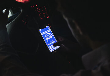 Nahaufnahme eines jungen Mannes, der die Helligkeit seines Handys im Auto bei Nacht einstellt - UUF17617