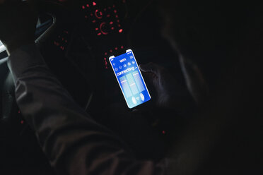 Close-up of young man connecting smartphone with wifi in car at night - UUF17619