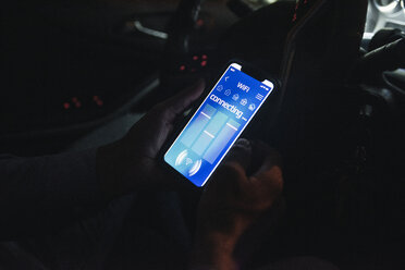 Nahaufnahme eines jungen Mannes, der sein Smartphone nachts im Auto mit dem Internet verbindet - UUF17620
