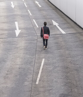 Rückansicht eines Geschäftsmannes, der auf einer Straße mit Pfeilschildern geht - UUF17624