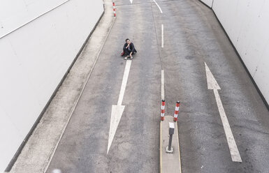 Geschäftsmann sitzend auf Straße mit Pfeilzeichen - UUF17638