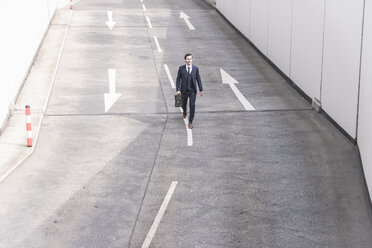 Businessman walking on road with arrow signs - UUF17641