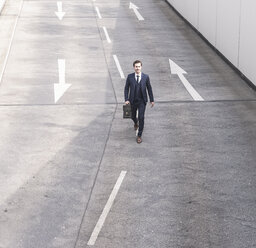 Businessman walking on road with arrow signs - UUF17642