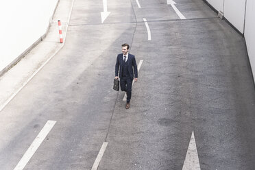 Businessman walking on road with arrow signs - UUF17643