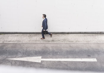 Businessman walking at road with arrow sign - UUF17645