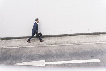 Businessman walking at road with arrow sign - UUF17646