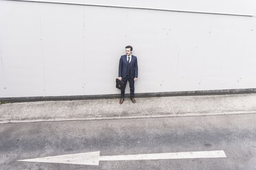 Businessman standing at road with arrow sign - UUF17647