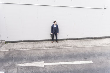 Businessman standing at road with arrow sign - UUF17648