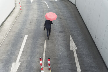 Rückansicht eines Geschäftsmannes mit Regenschirm, der auf einer Straße mit Pfeilschildern geht - UUF17649