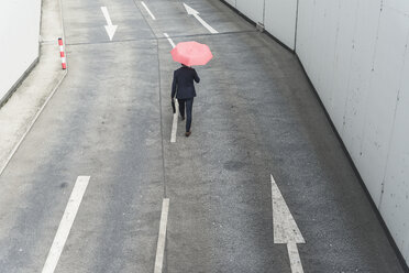 Rückansicht eines Geschäftsmannes mit Regenschirm, der auf einer Straße mit Pfeilschildern geht - UUF17650