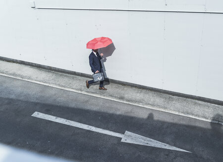 Businessman with umbrella walking at road with arrow sign - UUF17655