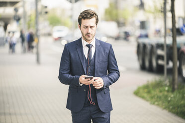 Businessman walking in the city using cell phone - UUF17682