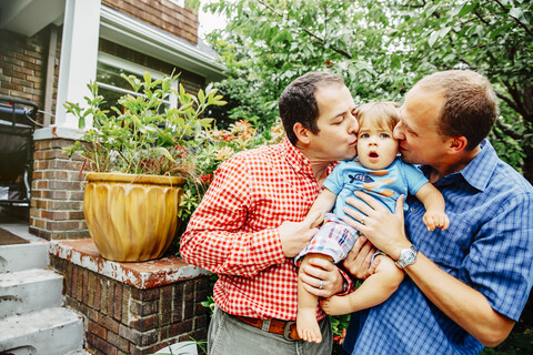 Gay fathers kissing baby son outdoors stock photo