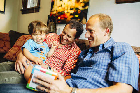 Schwule Väter spielen mit ihrem kleinen Sohn auf dem Sofa, lizenzfreies Stockfoto