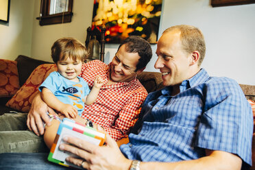 Gay fathers playing with baby son on sofa - BLEF03973