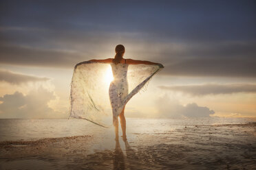 Caucasian woman holding fabric on beach at sunset - BLEF04059