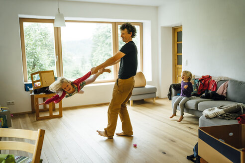 Caucasian father spinning daughter by arm and leg in livingroom - BLEF04160