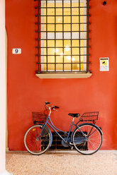 Blaues Fahrrad lehnt an orangefarbener Wand unter Fenster - BLEF04162