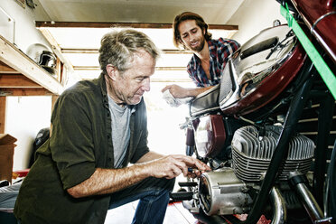 Kaukasischer Sohn beobachtet Vater bei der Reparatur eines Motorrads in der Garage - BLEF04215