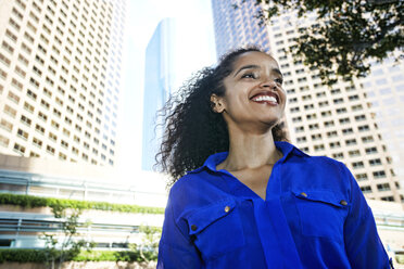 Smiling Hispanic businesswoman near highrises in city - BLEF04221