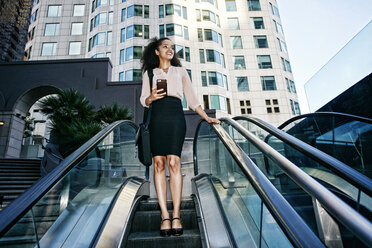 Smiling Hispanic businesswoman riding escalator outdoors - BLEF04229