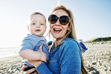 Smiling mother holding baby son at beach - BLEF04245