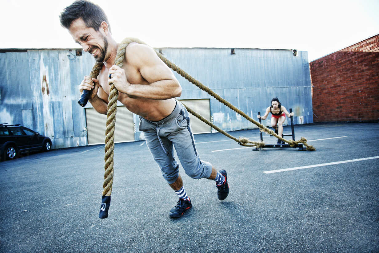 Caucasian man pulling woman with heavy ropes in parking lot outdoors stock  photo
