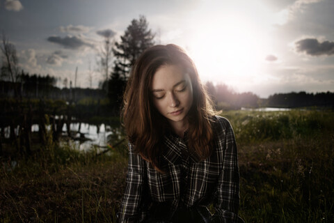 Nachdenkliche kaukasische Frau auf einem Feld in der Nähe eines Sees, lizenzfreies Stockfoto