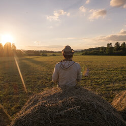 Mari Mann sitzt auf Heuballen bei Sonnenuntergang - BLEF04351