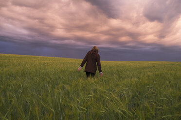 Sturmwolken über einer kaukasischen Frau, die in einem Feld mit hohem Gras spazieren geht - BLEF04358