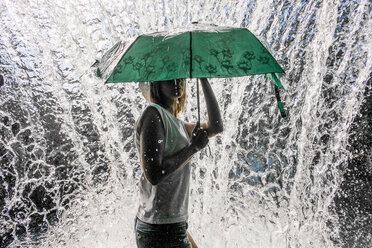 Kaukasische Frau hält Regenschirm in der Nähe von spritzendem Wasser - BLEF04365