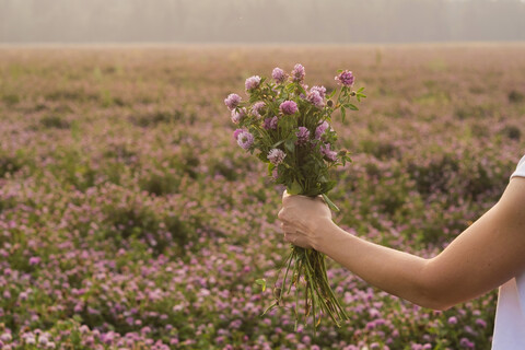 Kaukasische Frau hält Blumenstrauß im Feld, lizenzfreies Stockfoto