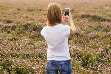 Kaukasische Frau fotografiert Blumenfeld mit Mobiltelefon - BLEF04387