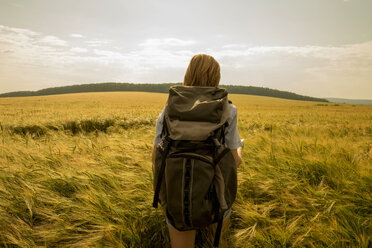 Caucasian woman walking in field carrying backpack - BLEF04396