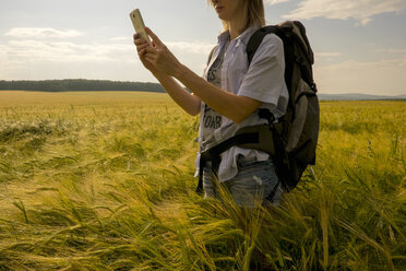 Kaukasische Frau steht auf einem Feld und benutzt ein Mobiltelefon - BLEF04397