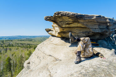 Caucasian man laying on mountain rock under blue sky - BLEF04410