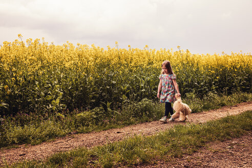 Mädchen geht allein mit Teddy und Rucksack auf einem Feldweg - SEBF00102