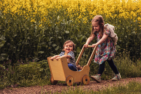 Mädchen mit ihrem Bruder in einem Puppenwagen auf einem Feldweg - SEBF00108