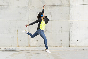 Woman with blue headphones listening music, jumping in the air - ERRF01364