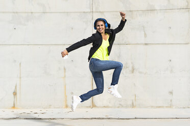 Woman with blue headphones listening music, jumping in the air - ERRF01365