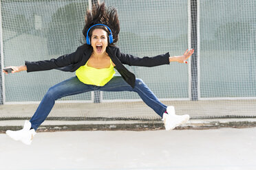 Woman with blue headphones listening music, jumping in the air - ERRF01367