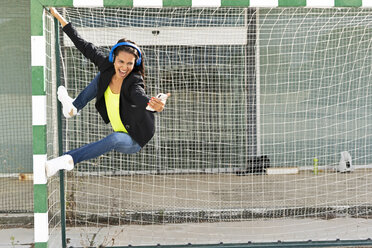 Woman with blue headphones listening music, hanging on goal - ERRF01369