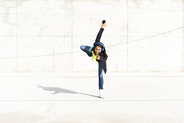 Woman with blue headphones listening music, standing on one leg - ERRF01370